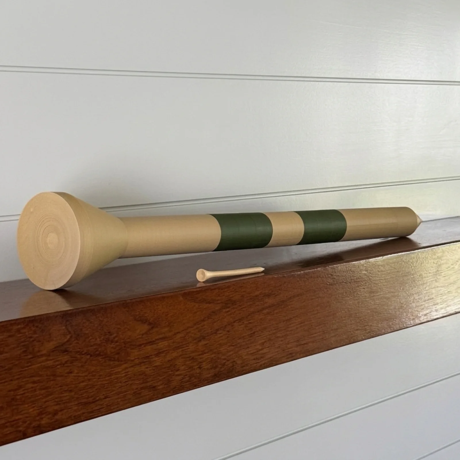 The Big Tee resting on a white mantle shelf with a standard golf tee beside it for scale