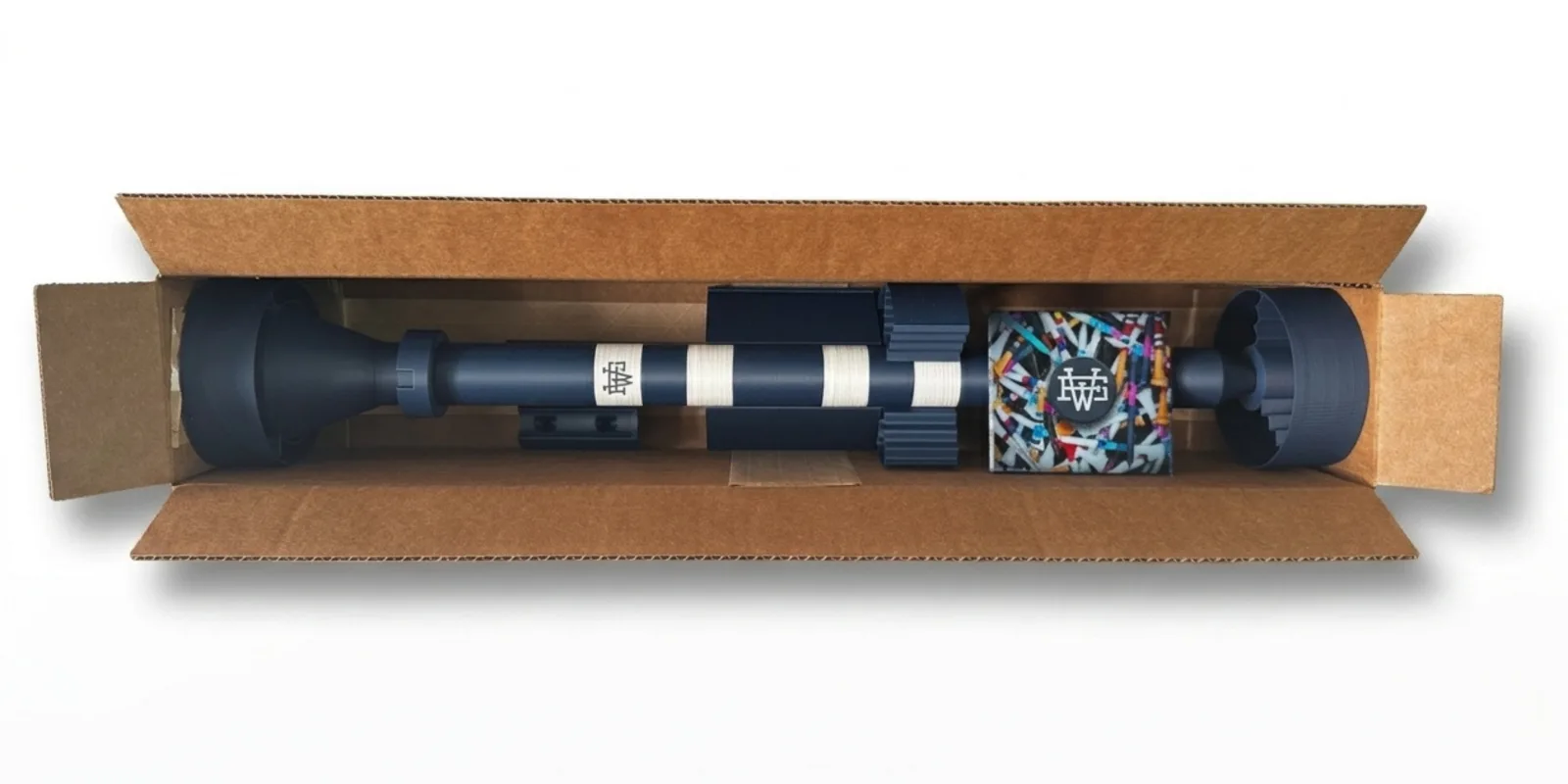The Big Tee packed inside its open shipping box, the cup and point seated in protective end caps, in Dark Blue with Ivory White rings